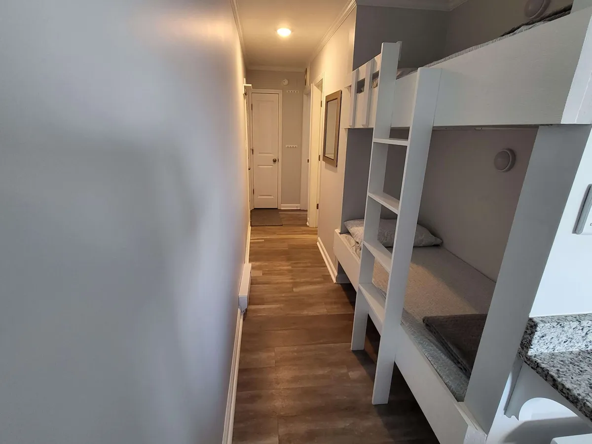 The photo features a set of custom-built bunk beds nestled in a cozy nook off a hallway, with warm lighting and soft bedding creating a secure and playful retreat for children. The setting exudes warmth and a family-friendly vibe.