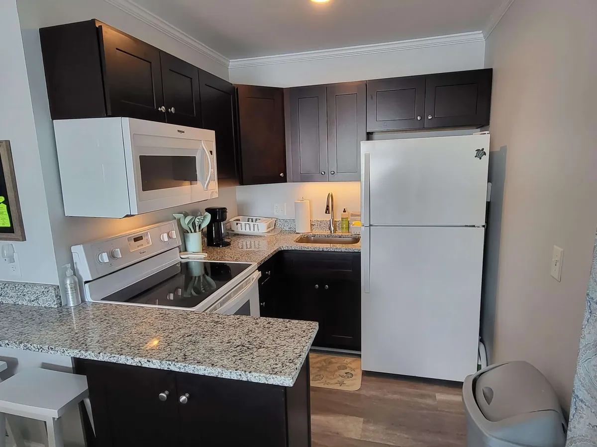 A cozy, inviting kitchen scene with dark wooden cabinets, white appliances, and a granite countertop. The open layout is perfect for gathering and meal prep, with a warm, home-like feel.